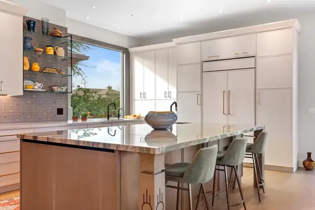 Troon, Scottsdale kitchen remodel with a veined stone island, sage counter stools, paneled refrigerator and a wide picture window