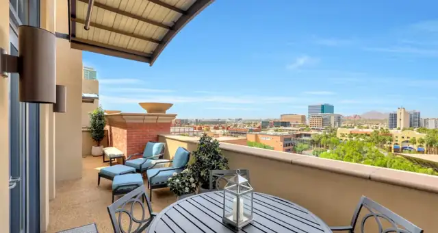 Covered outdoor balcony from a summer home remodel, with stucco walls, lounge chairs and a dining table overlooking the city