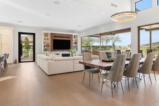 Open living and dining room redesign with a wide-plank wood floor, white sectional, built-in media wall, long dining table and glass walls to the patio