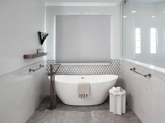 Bathroom with a freestanding tub and floor-mounted tub filler under a window, a patterned tile accent band and a gray stone floor