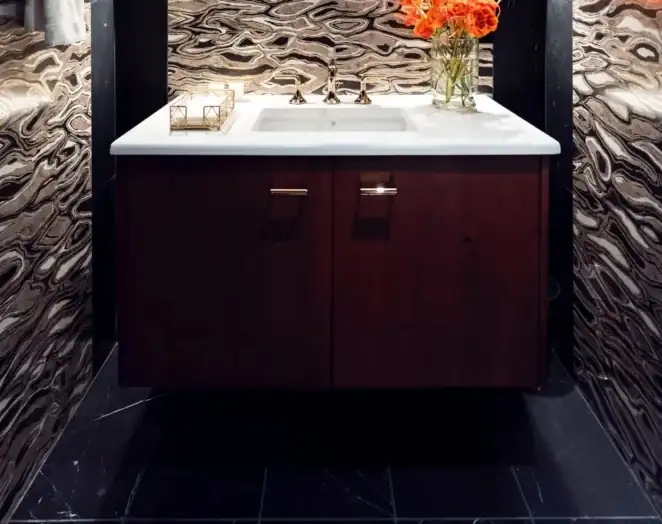 Powder room vanity with a white top on a dark wood cabinet against a swirled stone wall