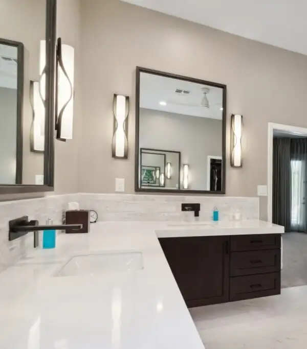 Miller primary bath with a white L-shaped vanity on dark wood cabinets, framed mirrors and sculpted wall sconces